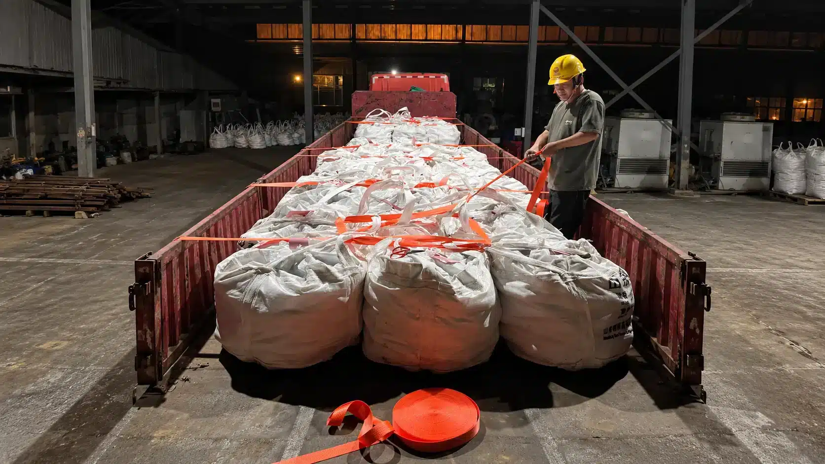 Transporte de bolas de moagem por caminhão na Shandong Gangyan: big bags brancos, cintas laranja e operador durante o carregamento.